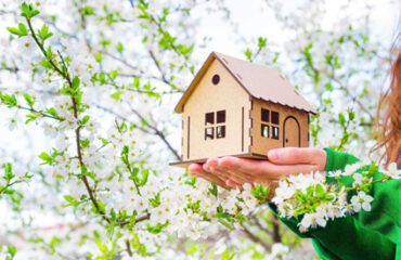 Maison miniature tenue dans les mains d'une femme au milieu d'un arbre en fleurs