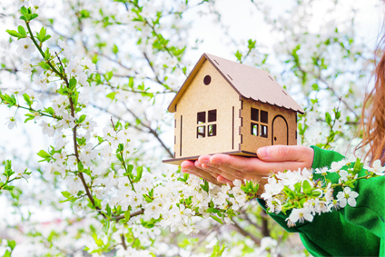 Maison miniature tenue dans les mains d'une femme au milieu d'un arbre en fleurs